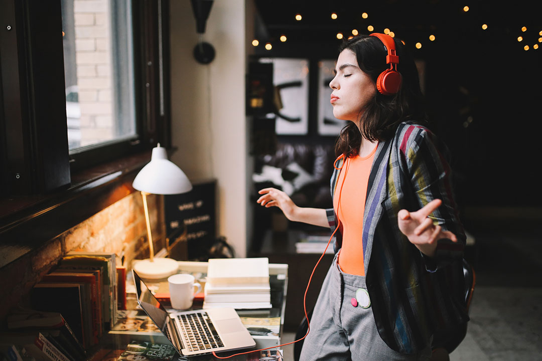 A young adult listening to music in her home. She has headphones on and is dancing.